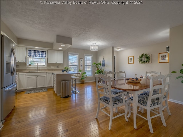 dining space with light hardwood / wood-style floors, a textured ceiling, sink, and a notable chandelier