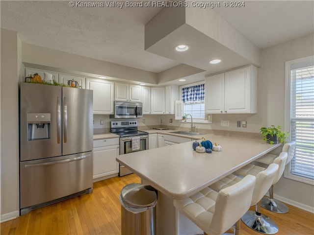 kitchen with kitchen peninsula, appliances with stainless steel finishes, sink, and white cabinets