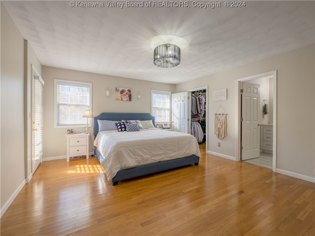 bedroom with a spacious closet, wood-type flooring, a notable chandelier, and ensuite bathroom