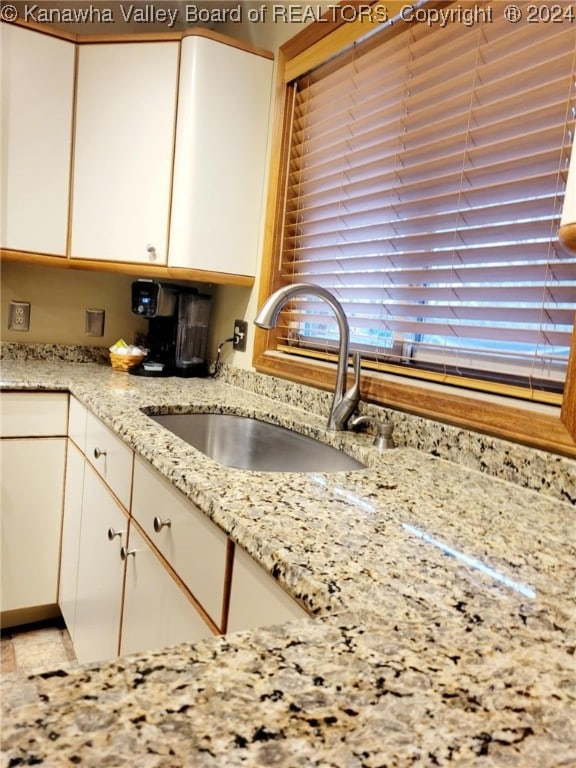 kitchen featuring light stone countertops, white cabinetry, and sink