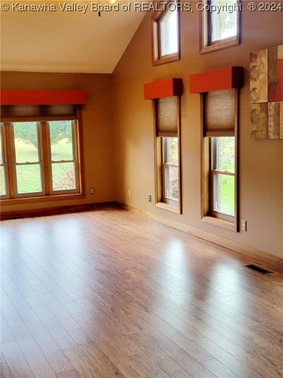 unfurnished room with a wealth of natural light, high vaulted ceiling, and light hardwood / wood-style floors