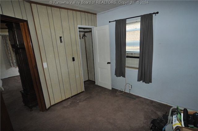 unfurnished bedroom featuring dark colored carpet, wood walls, crown molding, and a closet