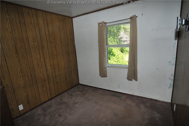 empty room with ornamental molding, wooden walls, and dark carpet