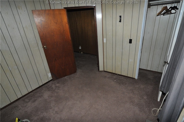 unfurnished bedroom with a closet, wooden walls, and dark colored carpet