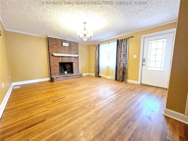 unfurnished living room with a chandelier, hardwood / wood-style floors, a brick fireplace, and a textured ceiling