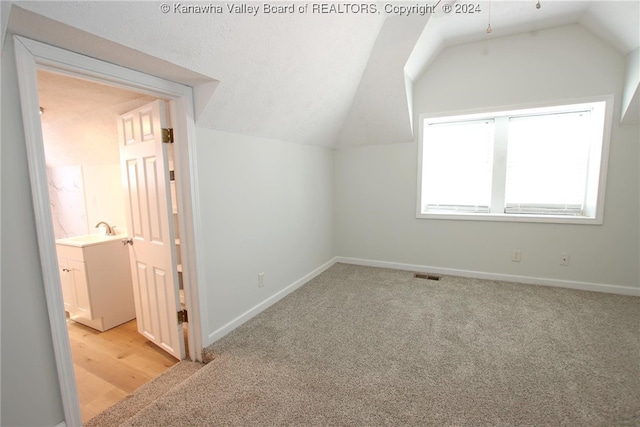 additional living space featuring light wood-type flooring, lofted ceiling, and sink