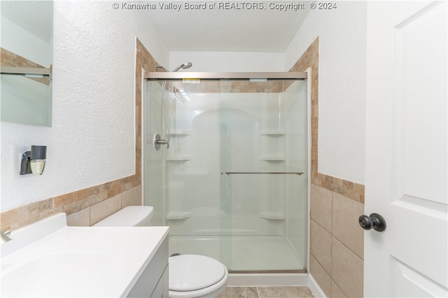 bathroom featuring toilet, tile walls, a textured ceiling, vanity, and a shower with shower door