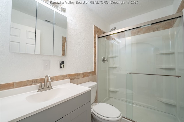 bathroom with toilet, vanity, a textured ceiling, and a shower with shower door