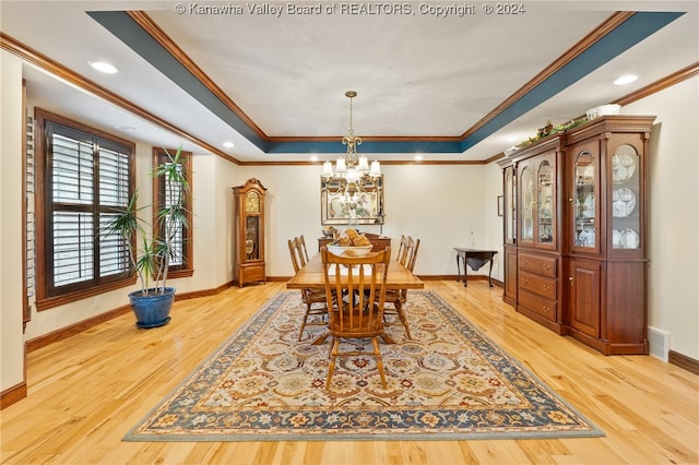 dining space with ornamental molding, an inviting chandelier, a tray ceiling, and light hardwood / wood-style floors