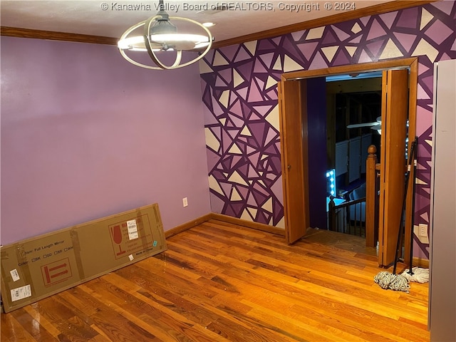 unfurnished room featuring wood-type flooring, ornamental molding, and an inviting chandelier