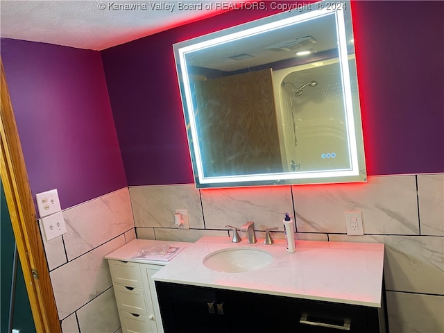 bathroom featuring tile walls, a shower, vanity, and a textured ceiling