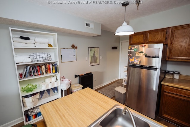 kitchen featuring a textured ceiling, decorative light fixtures, and stainless steel refrigerator