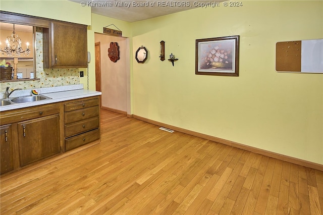 kitchen with light wood-type flooring, sink, hanging light fixtures, and a chandelier