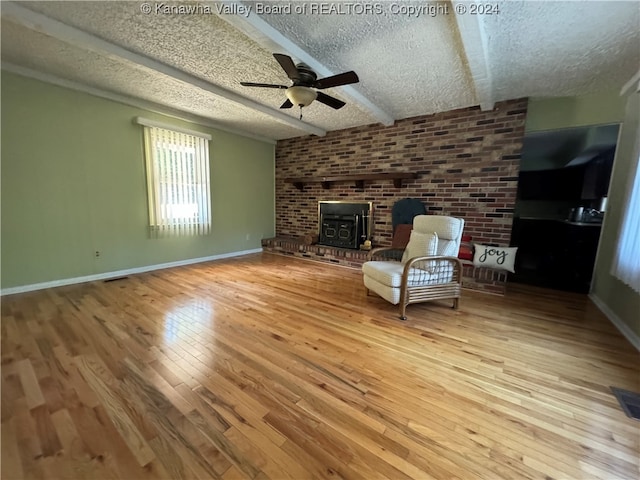 unfurnished room featuring a wood stove, ceiling fan, a textured ceiling, beam ceiling, and light hardwood / wood-style floors