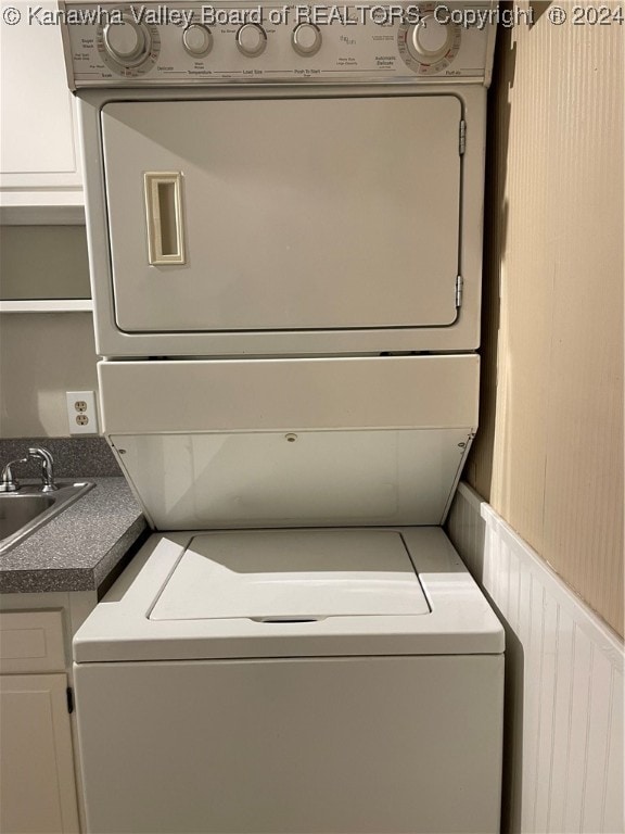 clothes washing area with cabinets, stacked washing maching and dryer, and sink