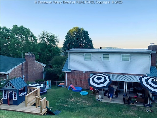 back house at dusk with a deck, a lawn, and a patio