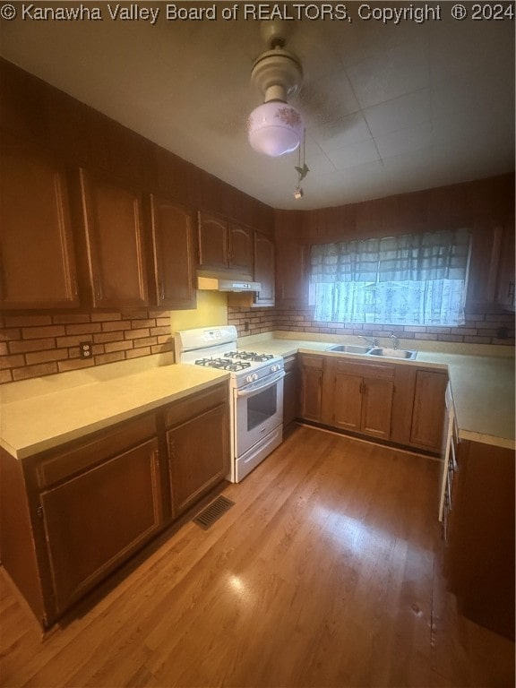 kitchen featuring light hardwood / wood-style floors, tasteful backsplash, gas range gas stove, and sink