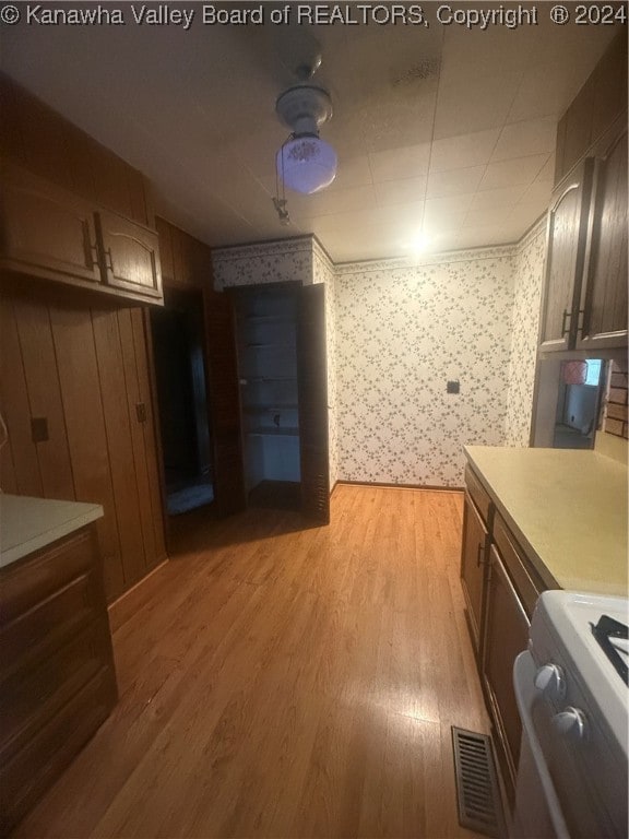 interior space with white range, light hardwood / wood-style floors, and wooden walls