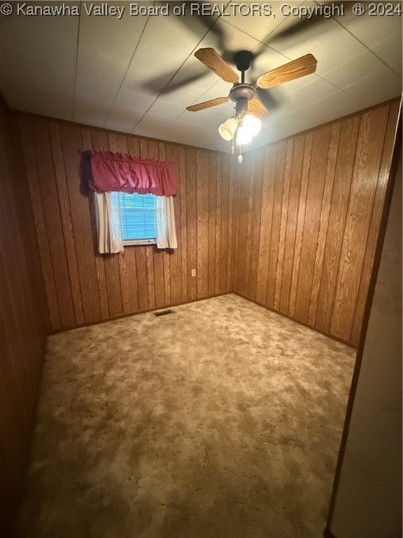 carpeted spare room featuring ceiling fan and wooden walls