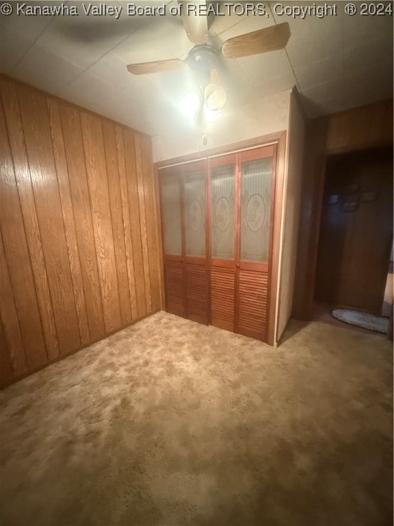 interior space with carpet flooring, ceiling fan, wooden walls, and a closet