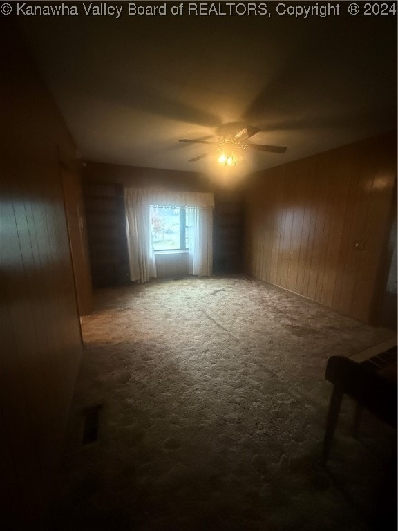 carpeted spare room featuring ceiling fan and wood walls