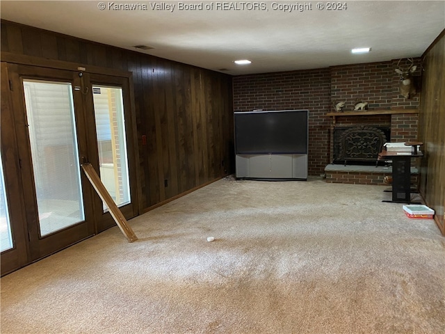 unfurnished living room with a fireplace, light colored carpet, and wood walls