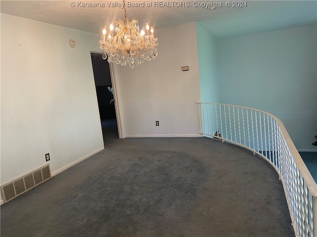 empty room with dark colored carpet and a notable chandelier