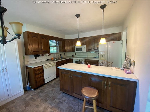 kitchen featuring a breakfast bar, white appliances, sink, decorative light fixtures, and dark brown cabinetry