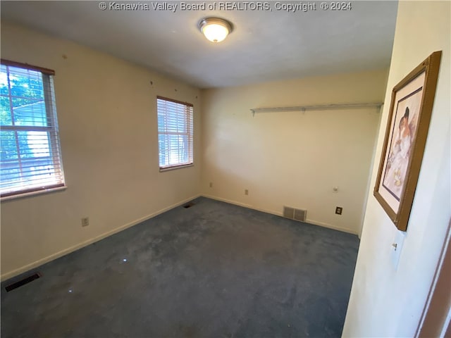 spare room with a wealth of natural light and dark colored carpet