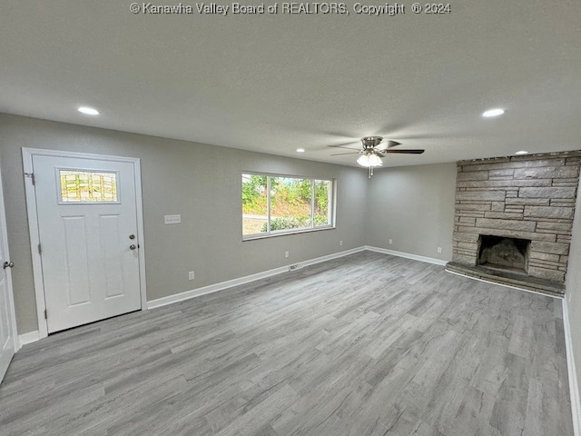 unfurnished living room with a stone fireplace, ceiling fan, light hardwood / wood-style flooring, and a textured ceiling