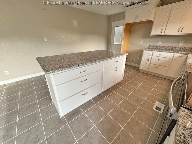 kitchen with white cabinetry, dark tile patterned floors, and light stone counters