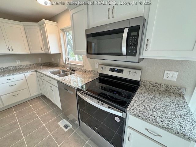 kitchen with light stone countertops, sink, stainless steel appliances, light tile patterned floors, and white cabinets