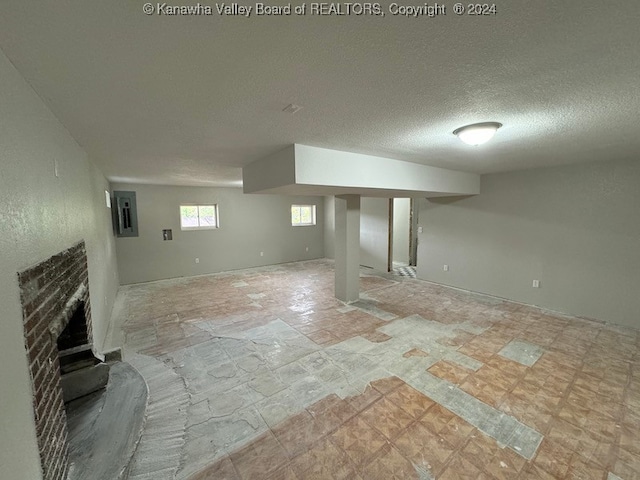 basement with a textured ceiling, electric panel, and a brick fireplace