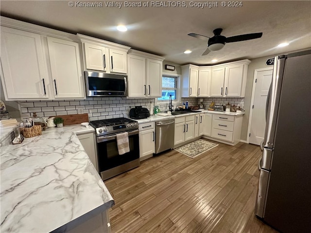 kitchen featuring appliances with stainless steel finishes, backsplash, sink, wood-type flooring, and white cabinets