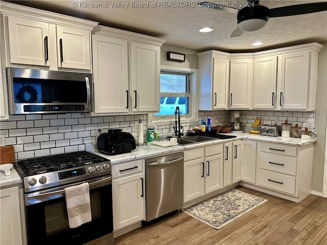 kitchen with decorative backsplash, a textured ceiling, stainless steel appliances, light hardwood / wood-style flooring, and white cabinetry