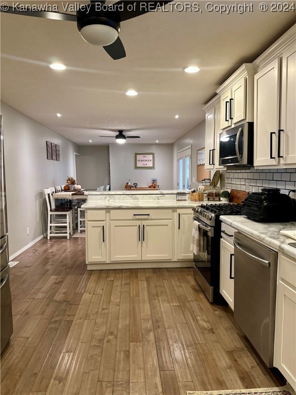 kitchen featuring kitchen peninsula, appliances with stainless steel finishes, light stone counters, light hardwood / wood-style floors, and white cabinetry