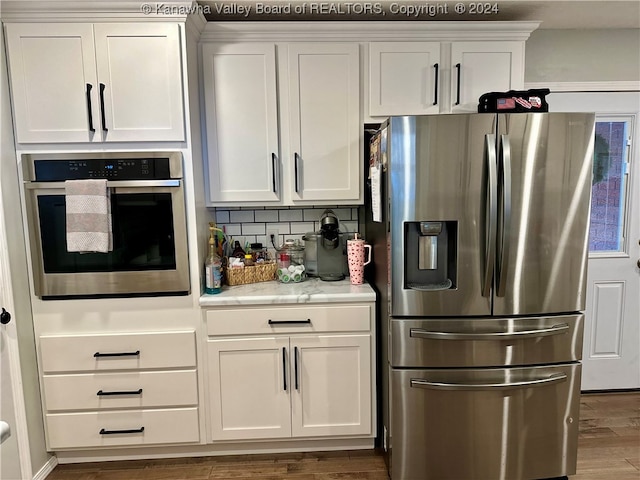 kitchen featuring tasteful backsplash, light stone counters, stainless steel appliances, dark wood-type flooring, and white cabinets