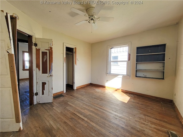 unfurnished room with a textured ceiling, dark hardwood / wood-style flooring, built in features, and ceiling fan