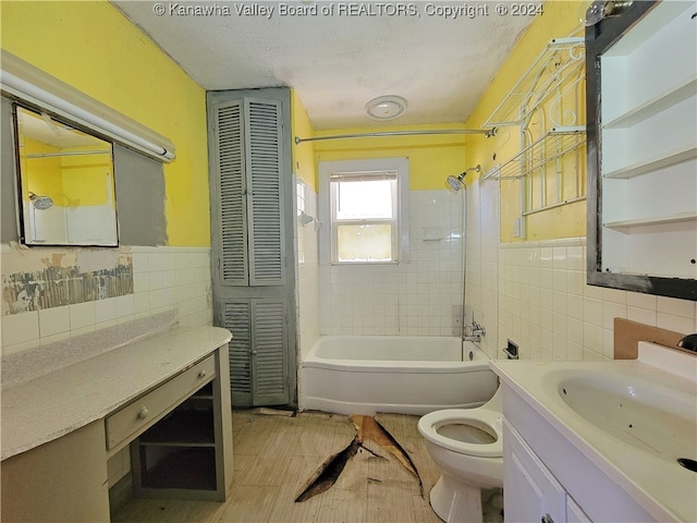 full bathroom featuring a textured ceiling, vanity, toilet, and tile walls