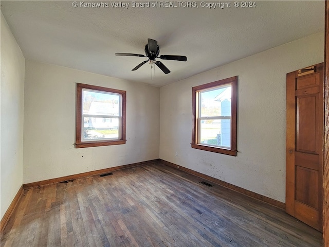 empty room with a textured ceiling, dark hardwood / wood-style flooring, plenty of natural light, and ceiling fan