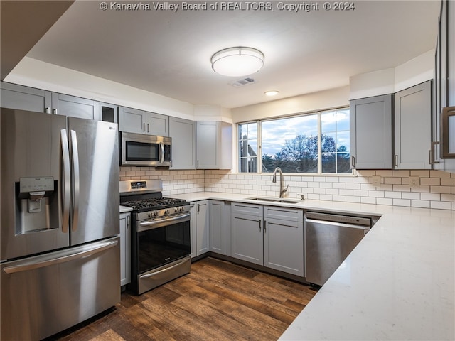 kitchen with gray cabinetry, dark wood-type flooring, sink, tasteful backsplash, and stainless steel appliances