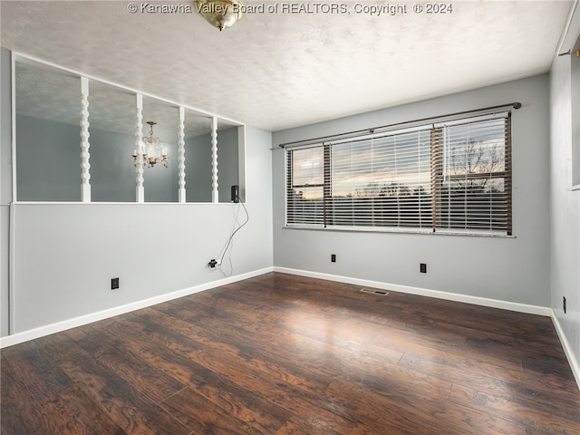 unfurnished room featuring a chandelier, a textured ceiling, and dark hardwood / wood-style floors