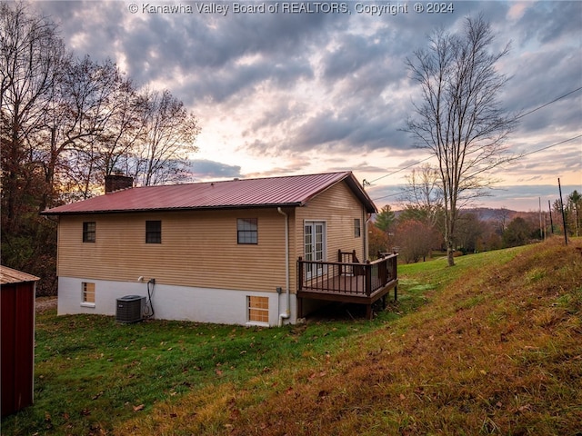 back house at dusk featuring central AC unit, a wooden deck, and a lawn