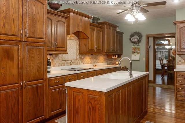 kitchen with dark wood-type flooring, a center island with sink, black electric stovetop, sink, and a textured ceiling