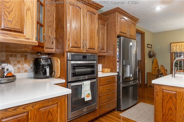 kitchen with backsplash, light hardwood / wood-style flooring, stainless steel appliances, and sink