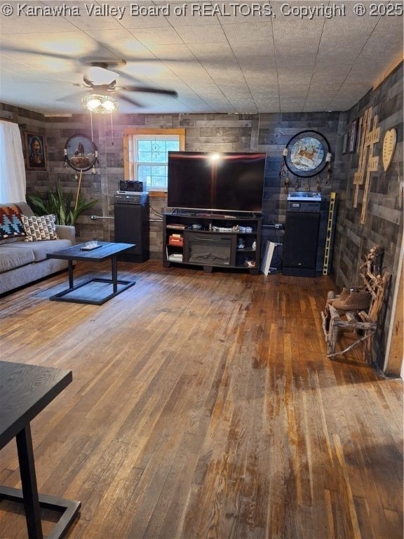 living room with hardwood / wood-style flooring, ceiling fan, and wood walls