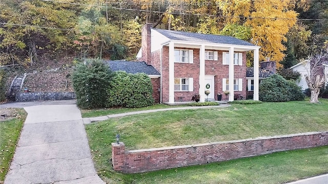 greek revival house with brick siding, a chimney, and a front lawn