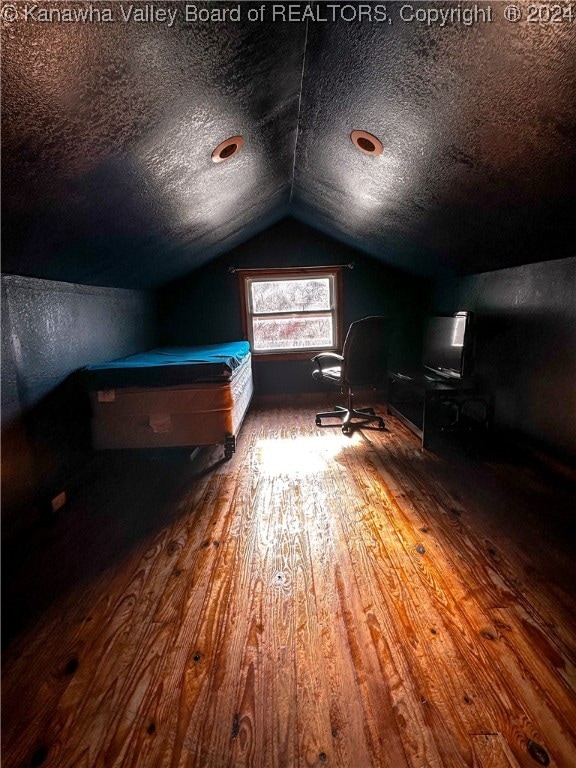 unfurnished bedroom featuring hardwood / wood-style floors, a textured ceiling, and vaulted ceiling