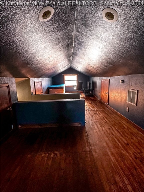 additional living space with a textured ceiling, dark hardwood / wood-style flooring, and lofted ceiling