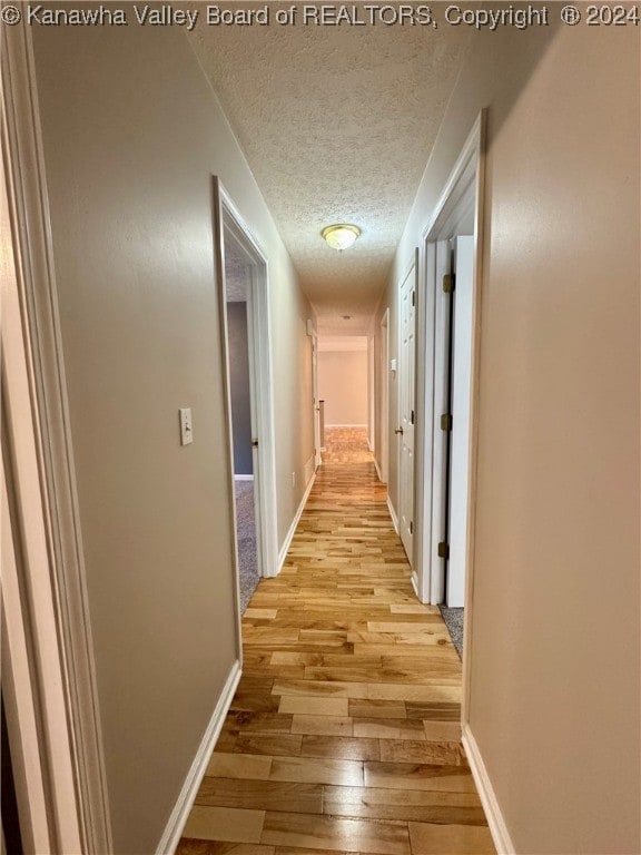 corridor featuring light wood-type flooring and a textured ceiling